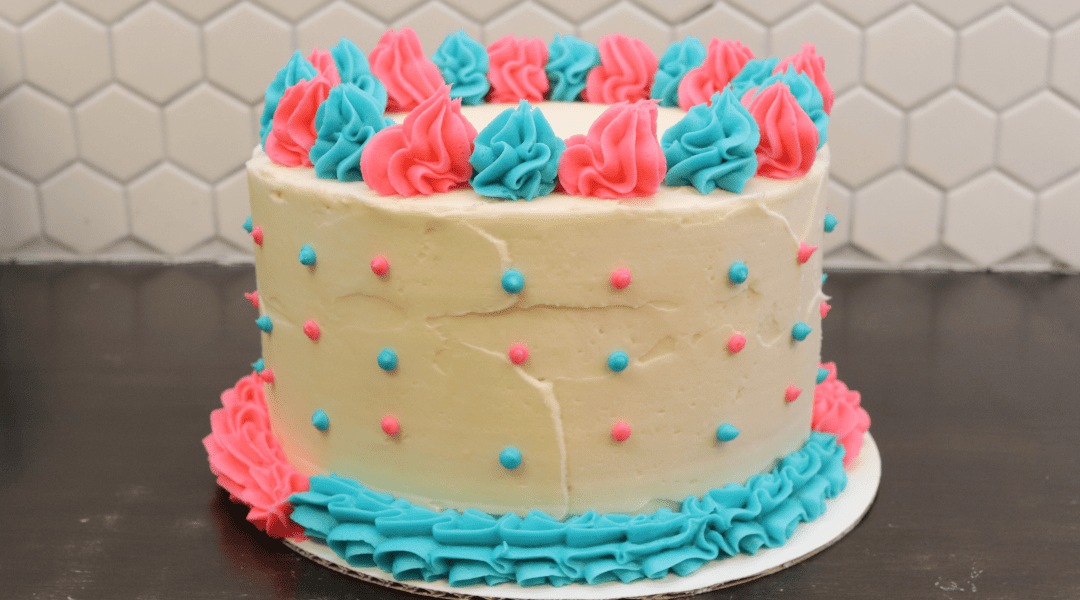 An adorable gender reveal custom cake has a the answer inside while the outside features blue and pink icing